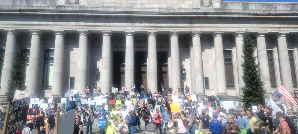 Group of people sitting in front of the Washington state Temple of Justice @ on the Capitol campus grpunds during the #handsoff protest